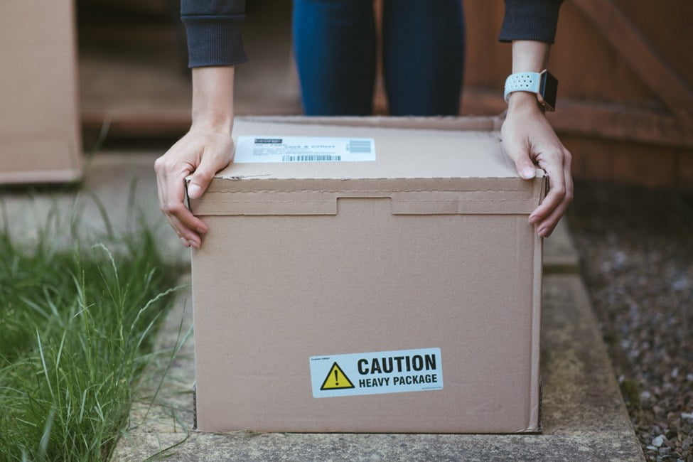 Person resting arms on box on the ground labelled as heavy package